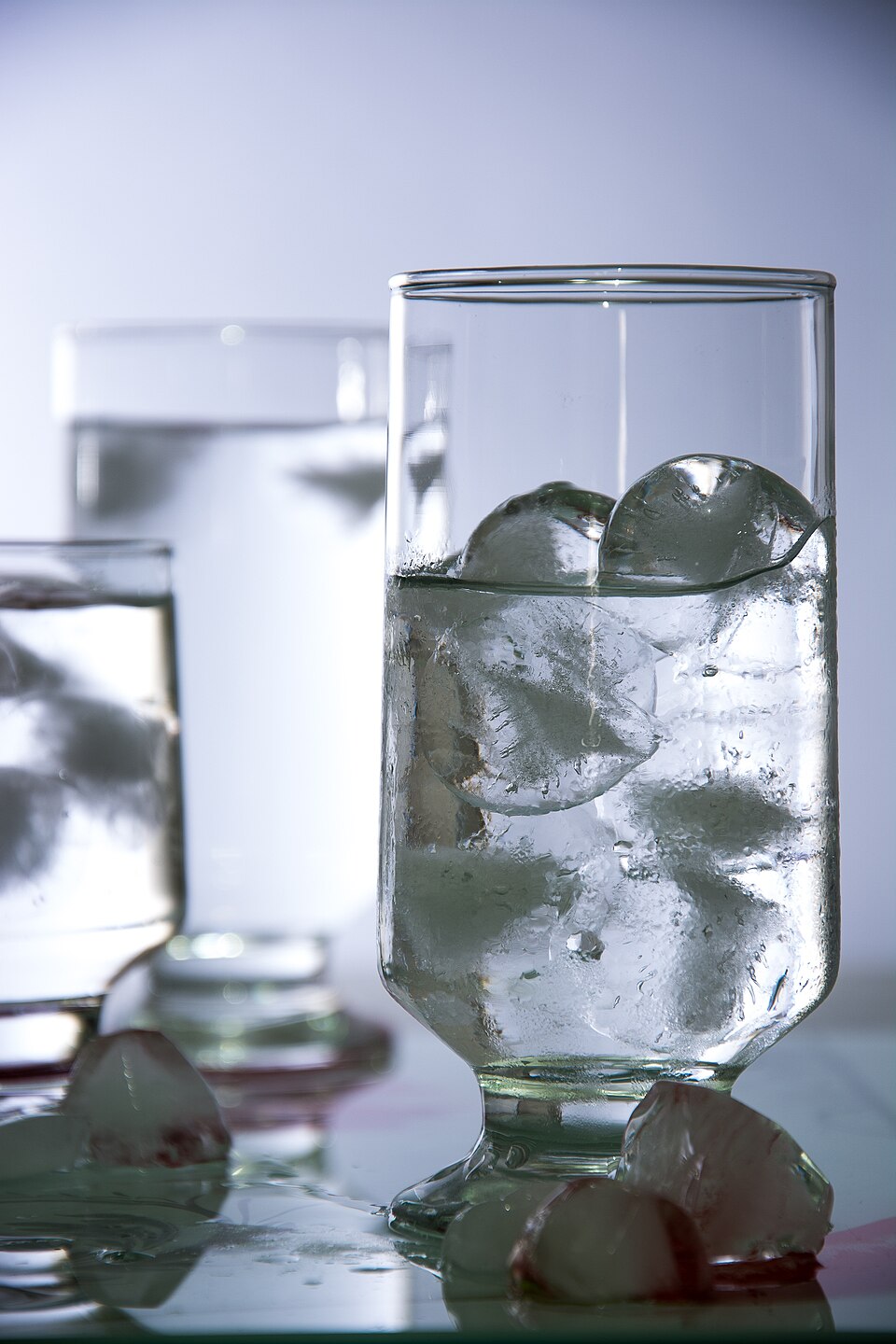 Ice cubes floating at the top of a tall glass of clear water, showing that solid ice is less dense than the liquid water it floats on
