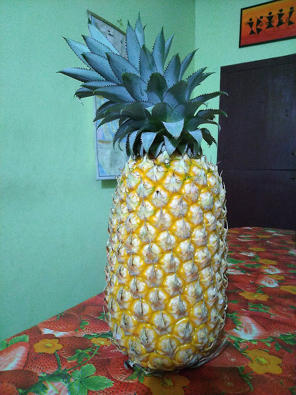 A whole ripe golden-yellow pineapple with its green spiky crown, standing upright on a table