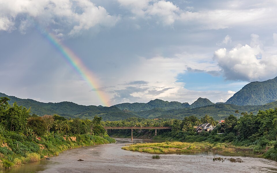 A primary rainbow arcing over a river valley and hills