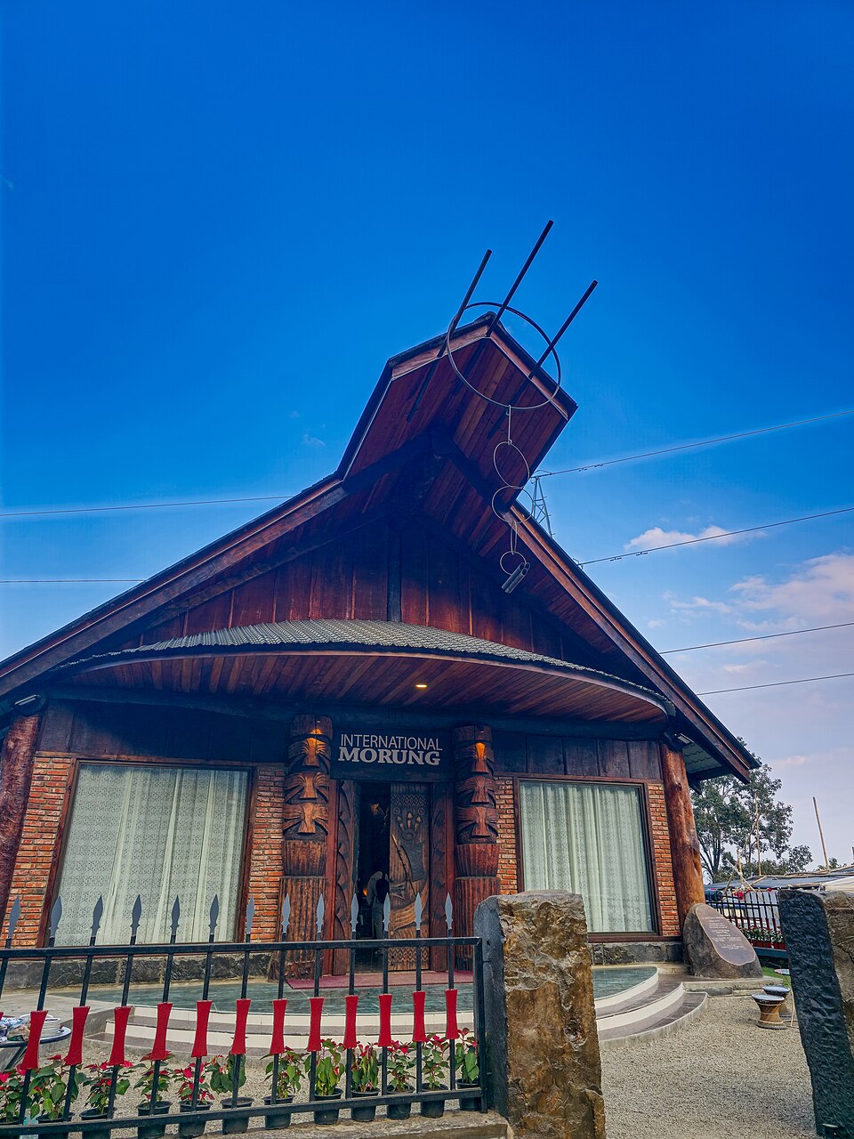 A traditional wooden Naga Morung communal house with carved posts and a crossed-horn gable at Kisama Heritage Village near Kohima, Nagaland