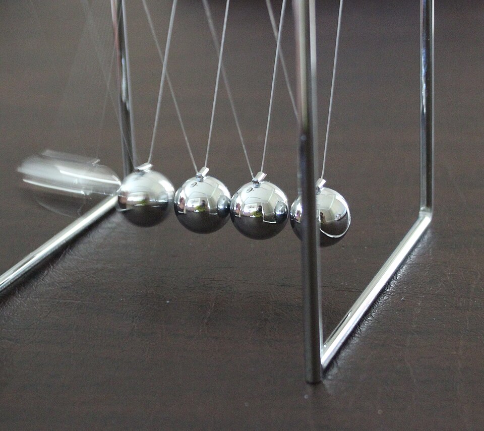 A Newton's cradle - identical polished steel balls suspended in a row from a metal frame, the classic demonstration of momentum transfer in an elastic collision