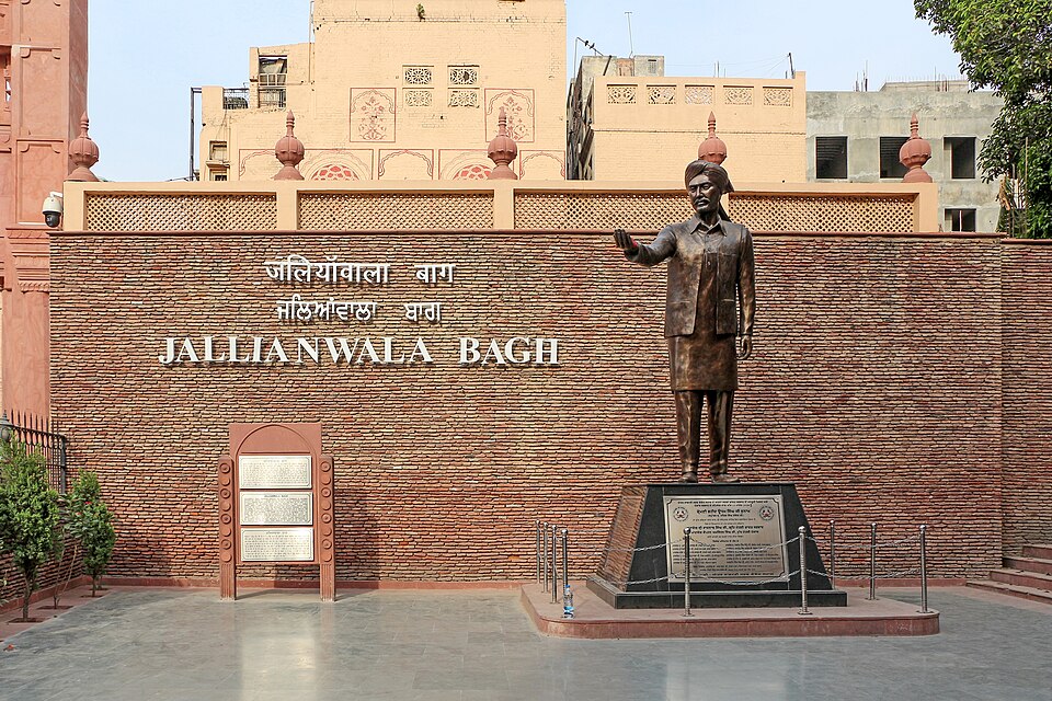 The Jallianwala Bagh memorial in Amritsar, its brick entrance wall carrying the site's name in Punjabi, Hindi and English beside a bronze statue