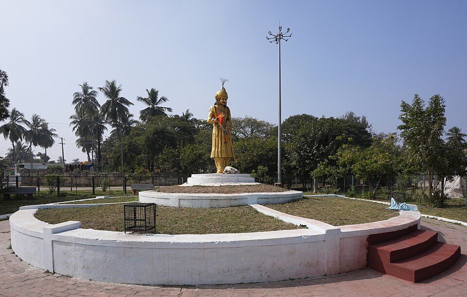 A tall golden statue of the Vijayanagara emperor Krishnadevaraya standing on a circular plinth in a garden at Anegundi, near Hampi
