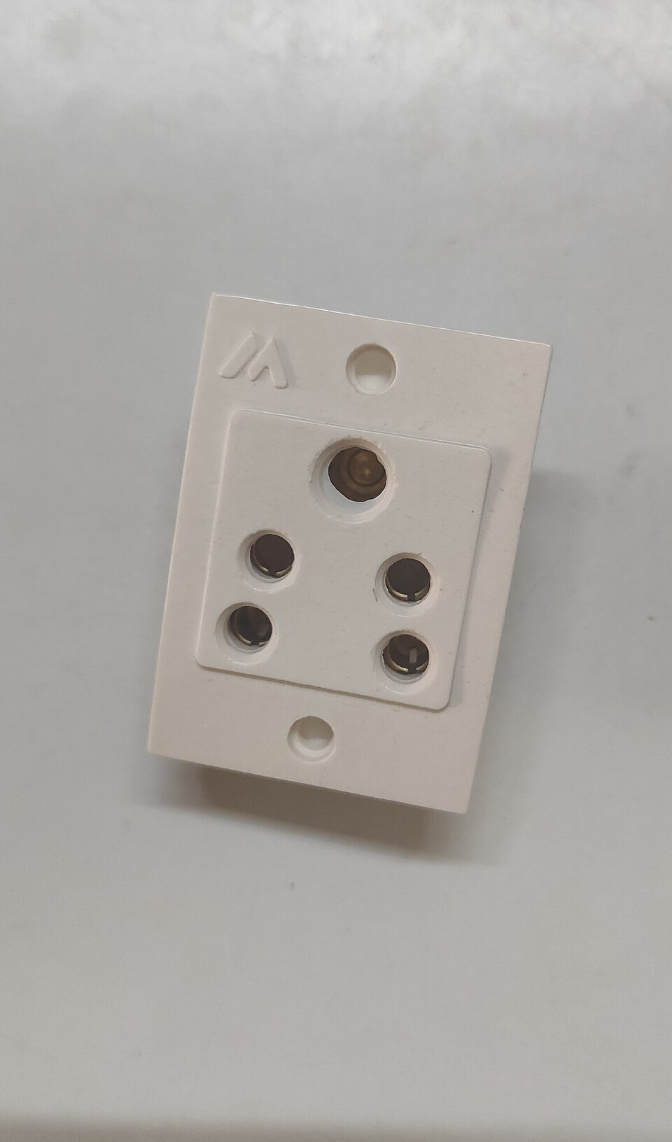 A white Indian domestic three-pin power socket with a large round earth pin hole above the line and neutral holes