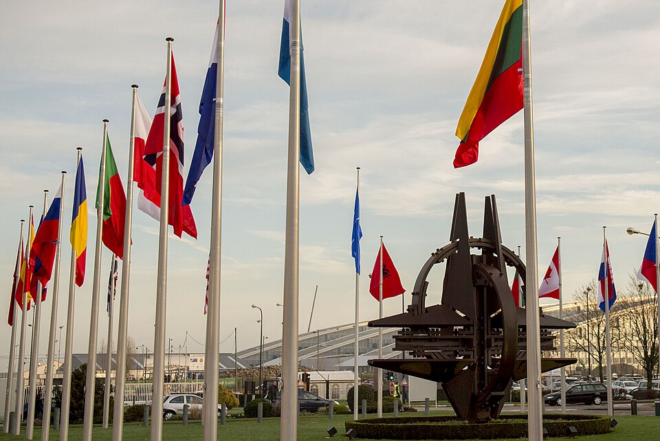 Member-state flags flying beside the NATO emblem sculpture at NATO Headquarters in Brussels