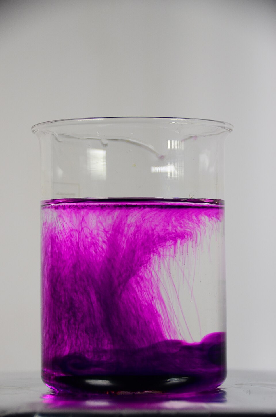 Purple potassium permanganate diffusing upward through still water in a glass beaker without stirring