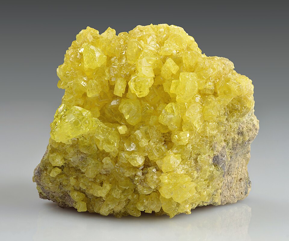 A specimen of native sulphur showing bright-yellow crystals on a rock matrix
