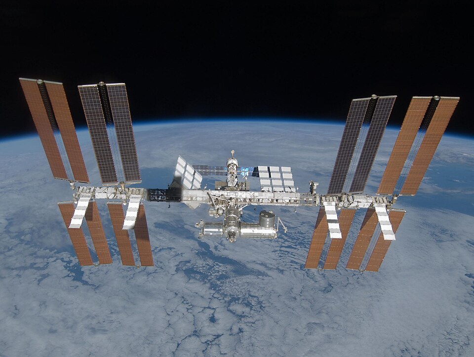 The International Space Station orbiting above the Earth, solar arrays extended against the blackness of space