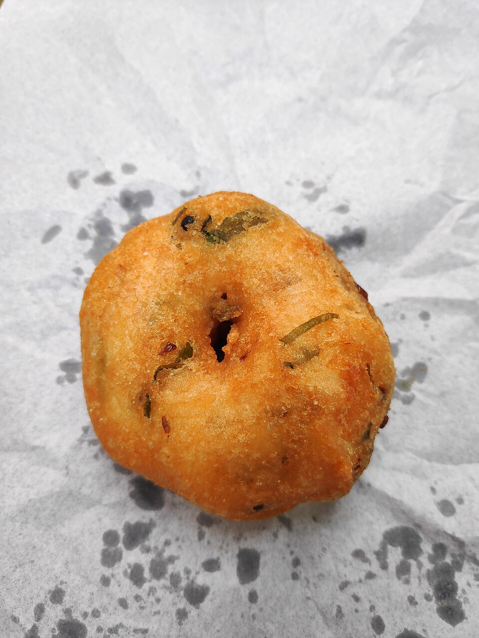 A deep-fried vada, a fatty fried snack, resting on paper