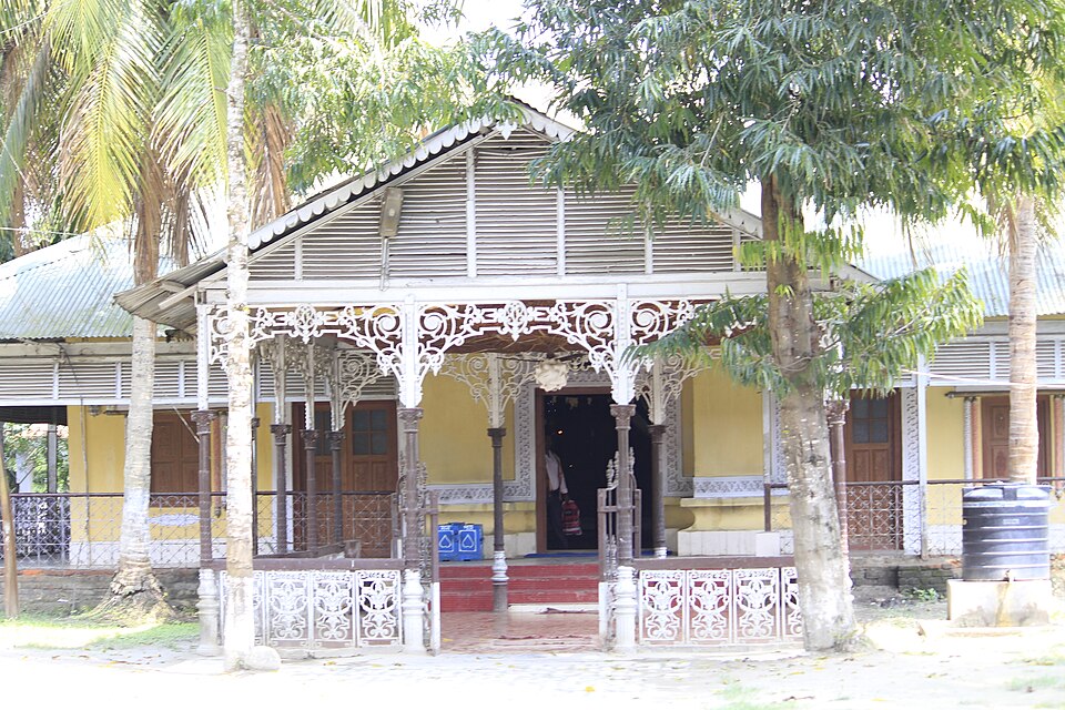 The namghar (Vaishnav prayer house) of Auniati Satra in Majuli, Assam, a tin-roofed hall with ornate white ironwork verandah