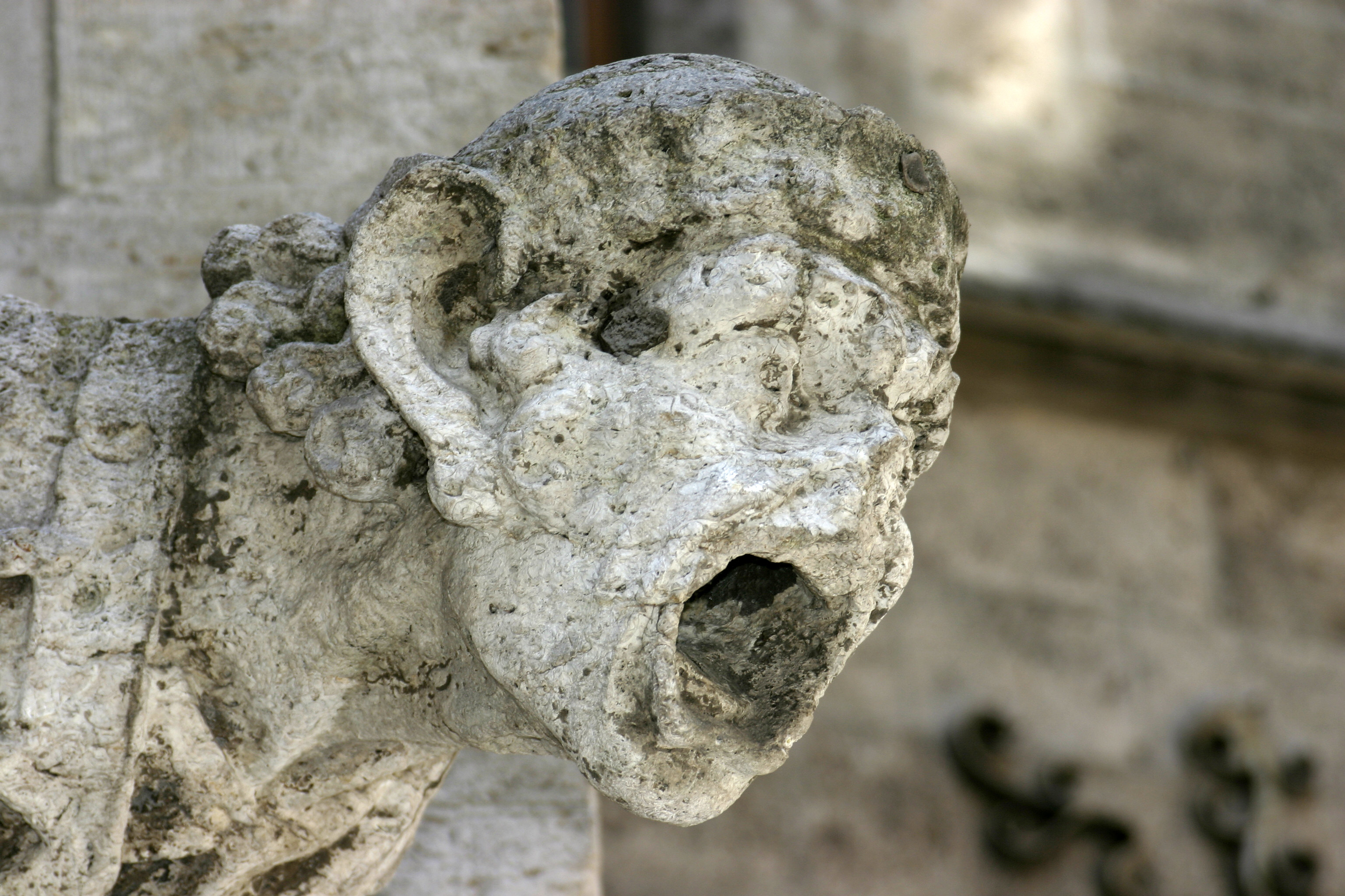 A carved stone gargoyle with its surface heavily corroded and pitted by acid rain, fine detail eaten away