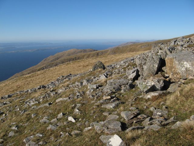 A periglacial blockfield of frost-shattered angular rock fragments strewn across a mountain slope above a loch