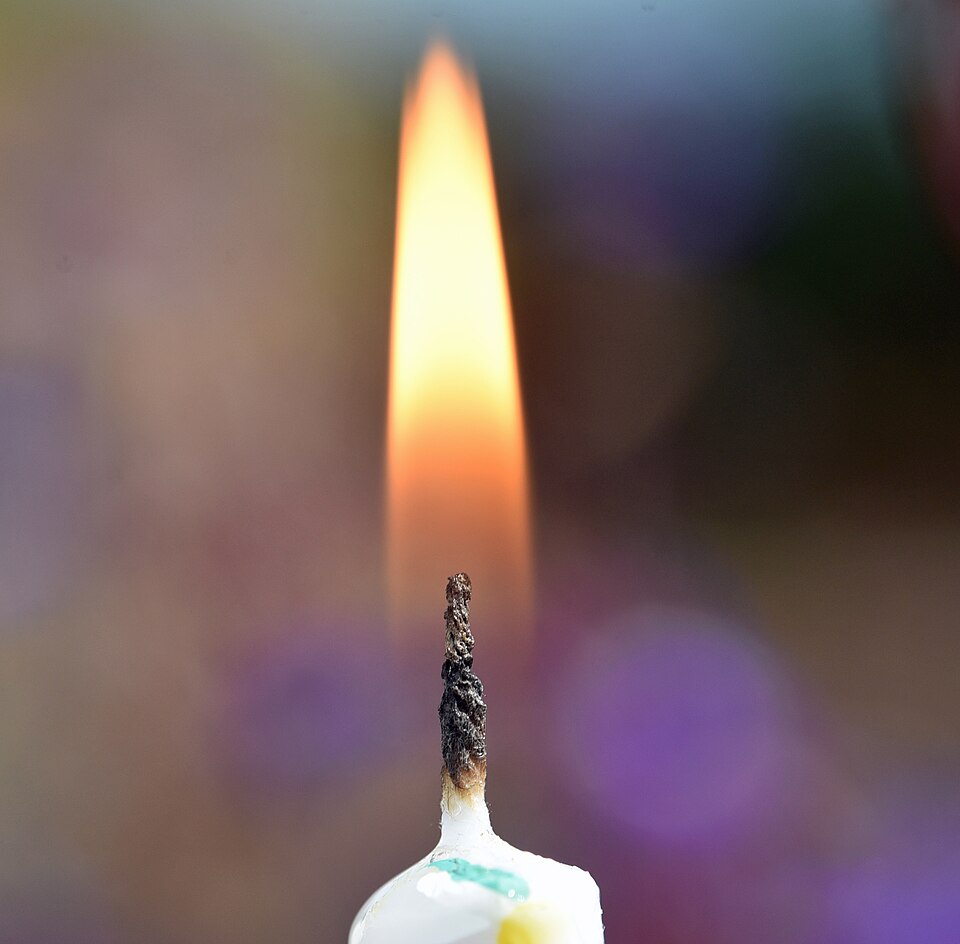 Close-up of a lit candle with a burning orange flame above the wick