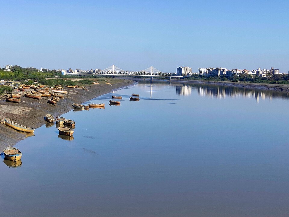 Wide view of the Tapti River at Surat with moored boats and a cable-stayed bridge in the distance