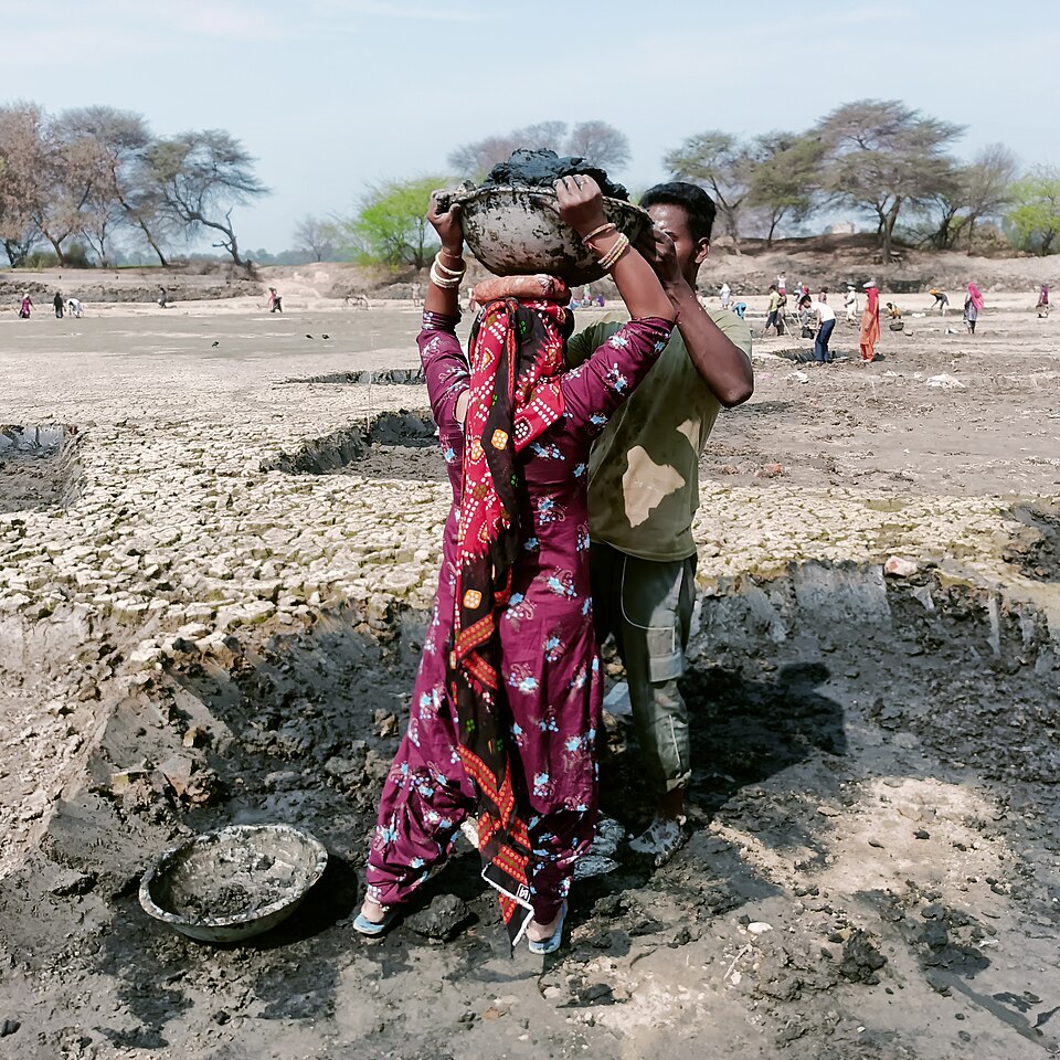 MGNREGA workers carrying baskets of mud while desilting a dry pond, a rural water-conservation earthwork