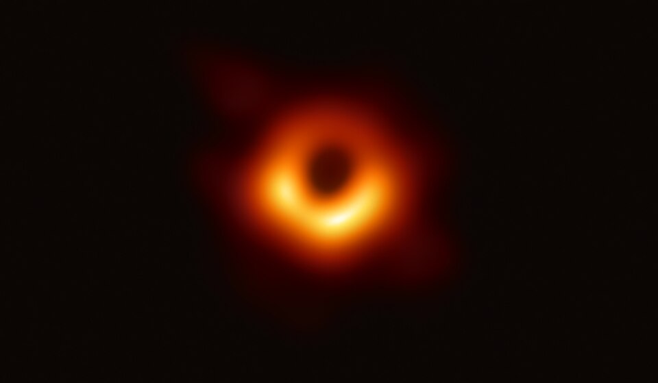 A blurred orange ring of light with a dark circular void at its centre, brightest along the lower edge, set against black space — the Event Horizon Telescope image of the M87 black hole.