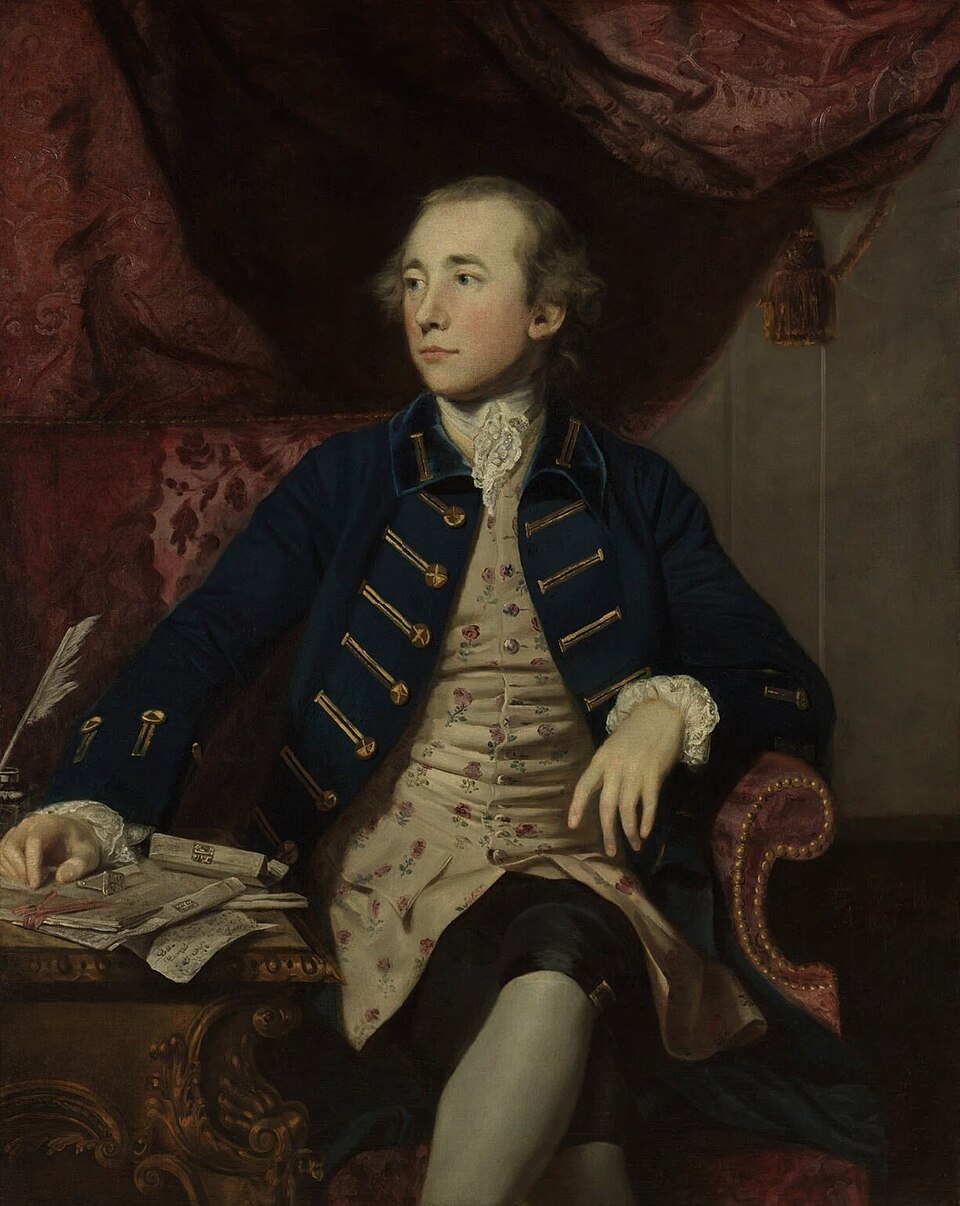An eighteenth-century oil portrait of Warren Hastings seated in a red upholstered chair, wearing a dark blue coat with gold frogging over a floral waistcoat, one hand resting on a desk strewn with papers and a quill