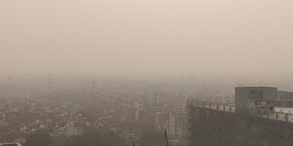 Thick grey smog blankets the Delhi cityscape, with rooftops and distant buildings fading into haze