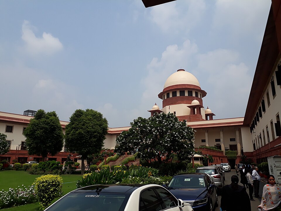 The red-sandstone and cream domed central block of the Supreme Court of India building in New Delhi, seen from its garden forecourt
