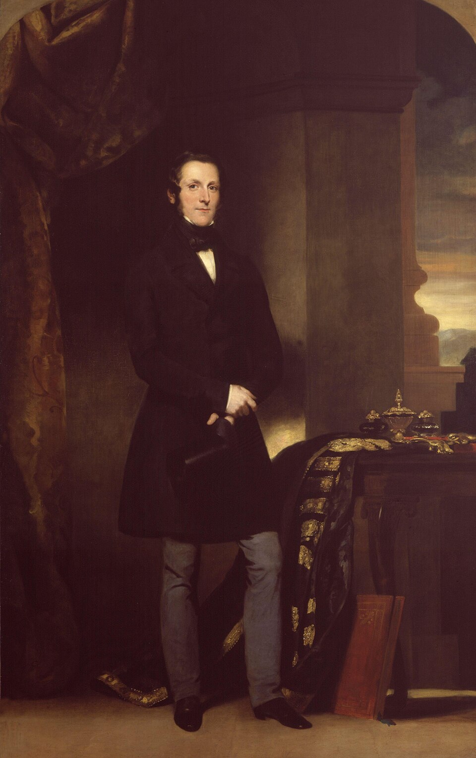 Full-length oil portrait of a man in a dark frock coat and grey trousers standing beside a table draped with a robe of state and gold regalia
