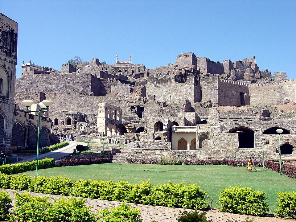 The tiered stone ramparts and ruined structures of Golconda Fort rising on a rocky hill above a manicured green garden