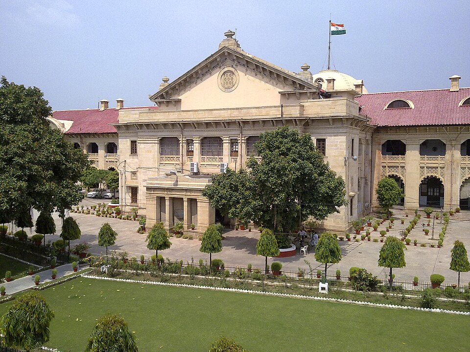 The colonial-era sandstone main building of the Allahabad High Court with a triangular pediment, red-tiled roofs and gardens, an Indian tricolour flag flying above