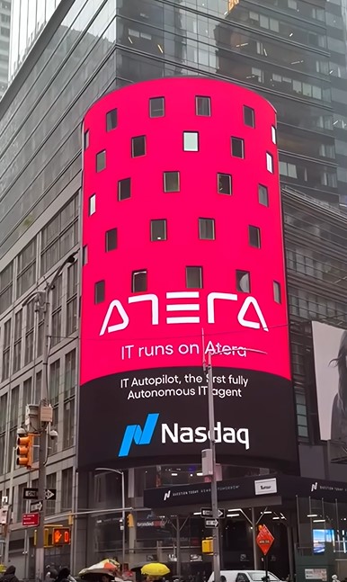 The cylindrical NASDAQ MarketSite LED billboard tower at Times Square, New York, displaying the Nasdaq logo and a pink advertisement above a street corner