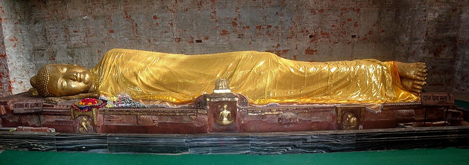 A large gilded reclining statue of the Buddha in the parinirvana pose, draped in a golden robe on a pedestal inside the Mahaparinirvana Temple at Kushinagar
