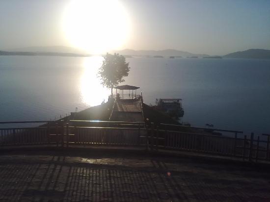 A broad reservoir at sunrise with low hills on the far shore and a jetty with a moored boat in the foreground