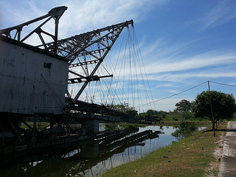 A large steel bucket-line tin-mining dredge standing in a water-filled mining pond in the Kinta Valley, Malaysia