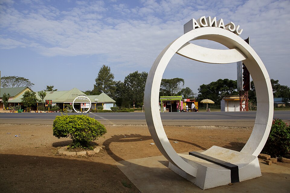 A large white circular monument reading UGANDA marking the Equator crossing at Kayabwe, with a matching smaller equator ring sign across the road