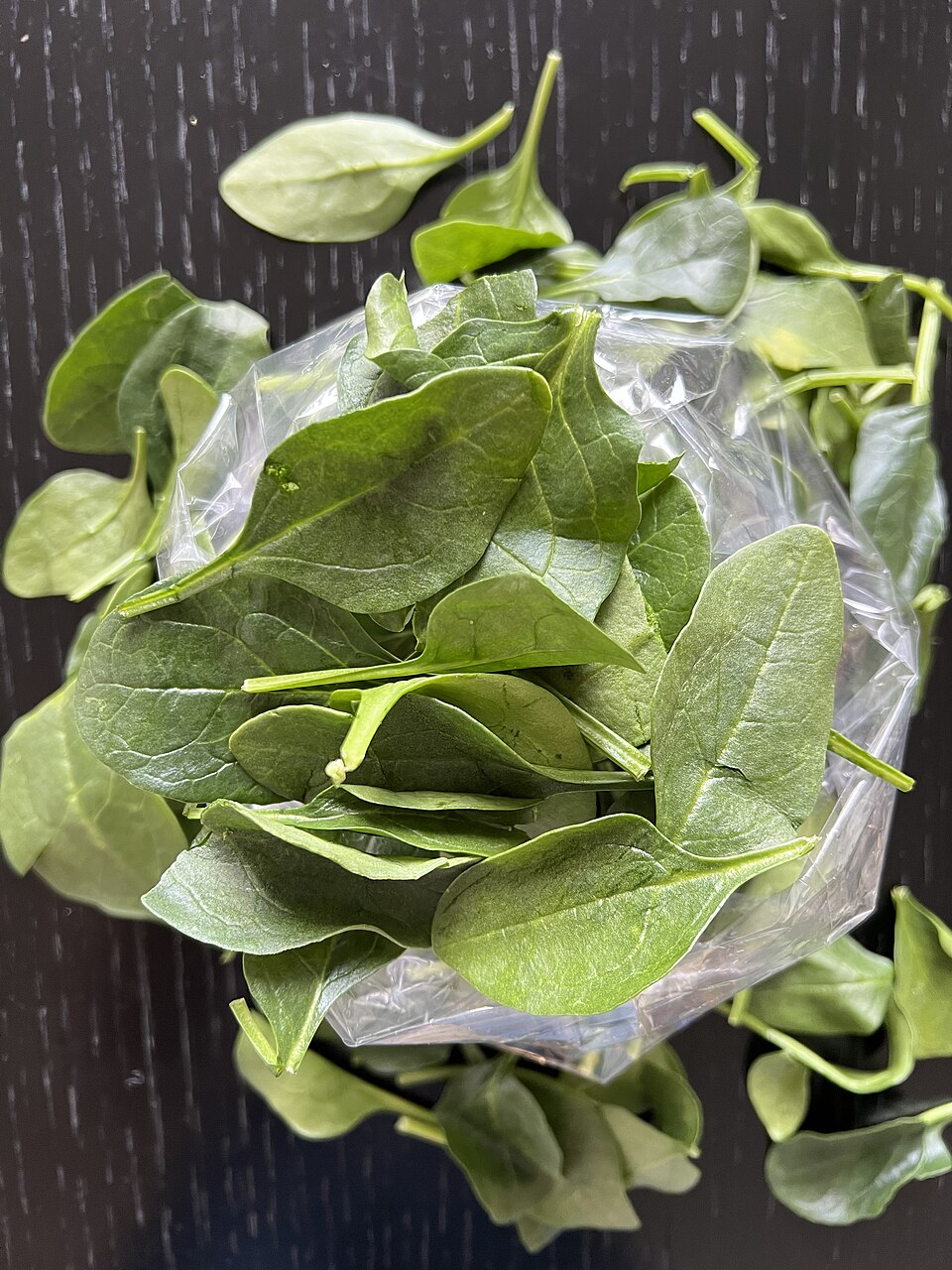 Fresh green baby spinach leaves spread on a dark surface