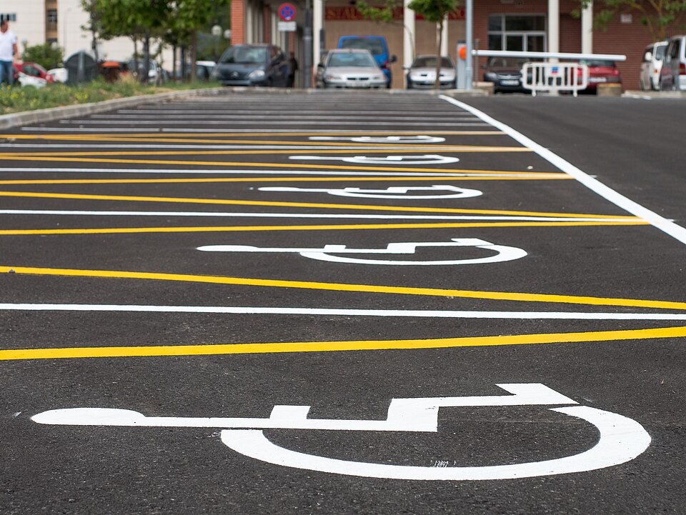 An asphalt car park with the white wheelchair accessibility symbol painted large in several reserved parking bays.