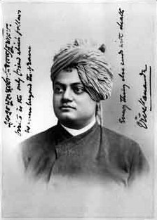 A black-and-white portrait photograph of a man in a turban and robe with his arms folded, with handwritten text beside him.