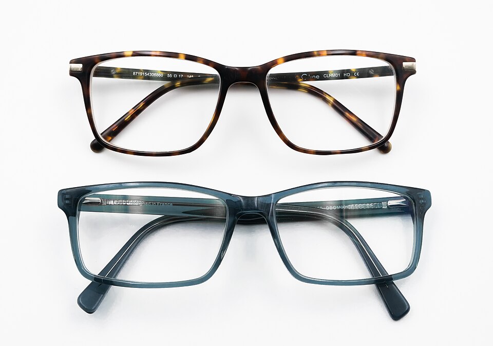 Two pairs of eyeglasses fitted with clear corrective lenses, one tortoiseshell frame and one blue frame, laid on a white surface.