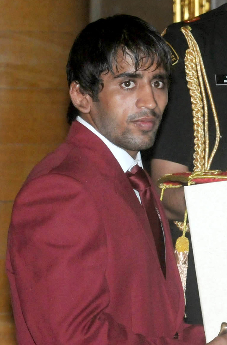 Wrestler Bajrang Punia in a maroon blazer and tie holding an award folder at a ceremony.