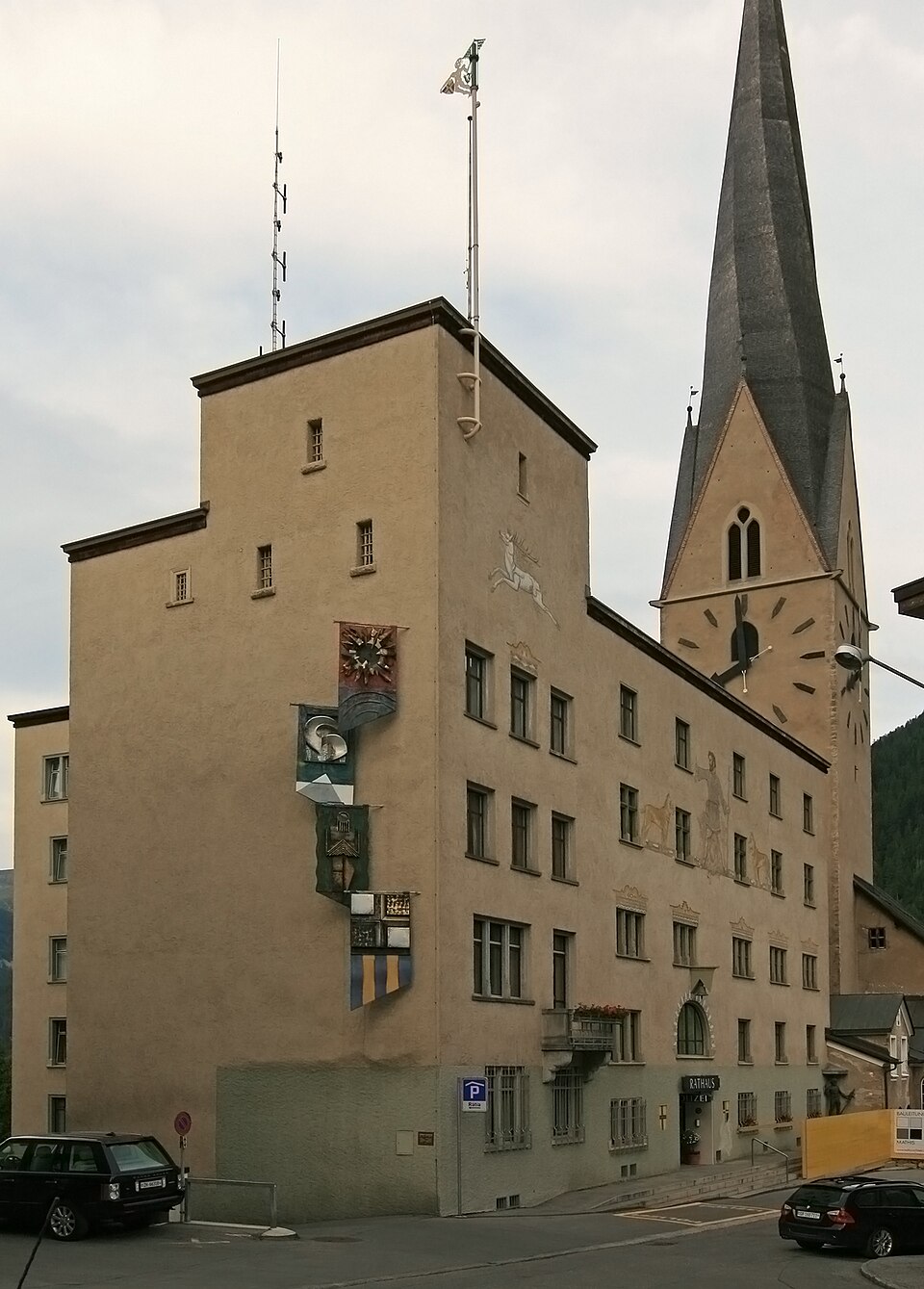 The town hall (Rathaus) of Davos, Switzerland, a tall Alpine building decorated with painted murals, standing beside a church steeple.