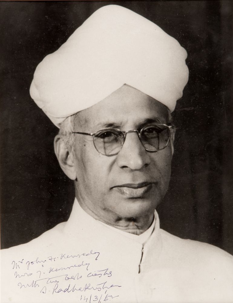 A black-and-white portrait of an elderly bespectacled man wearing a white turban and white jacket, with a handwritten dedication at the bottom.