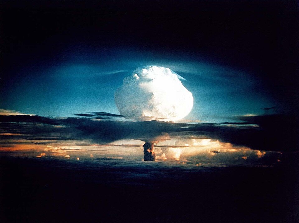 A huge glowing white mushroom cloud from a thermonuclear explosion rising over the ocean horizon at dusk.