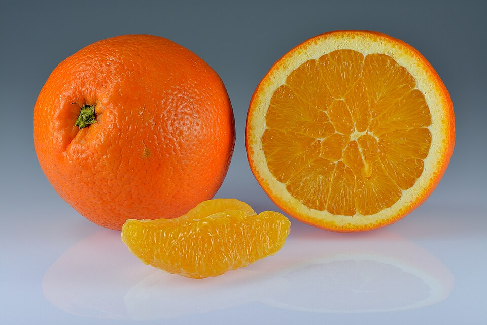 A whole unpeeled orange next to a halved orange showing its juicy segmented flesh, with two peeled segments resting in front.