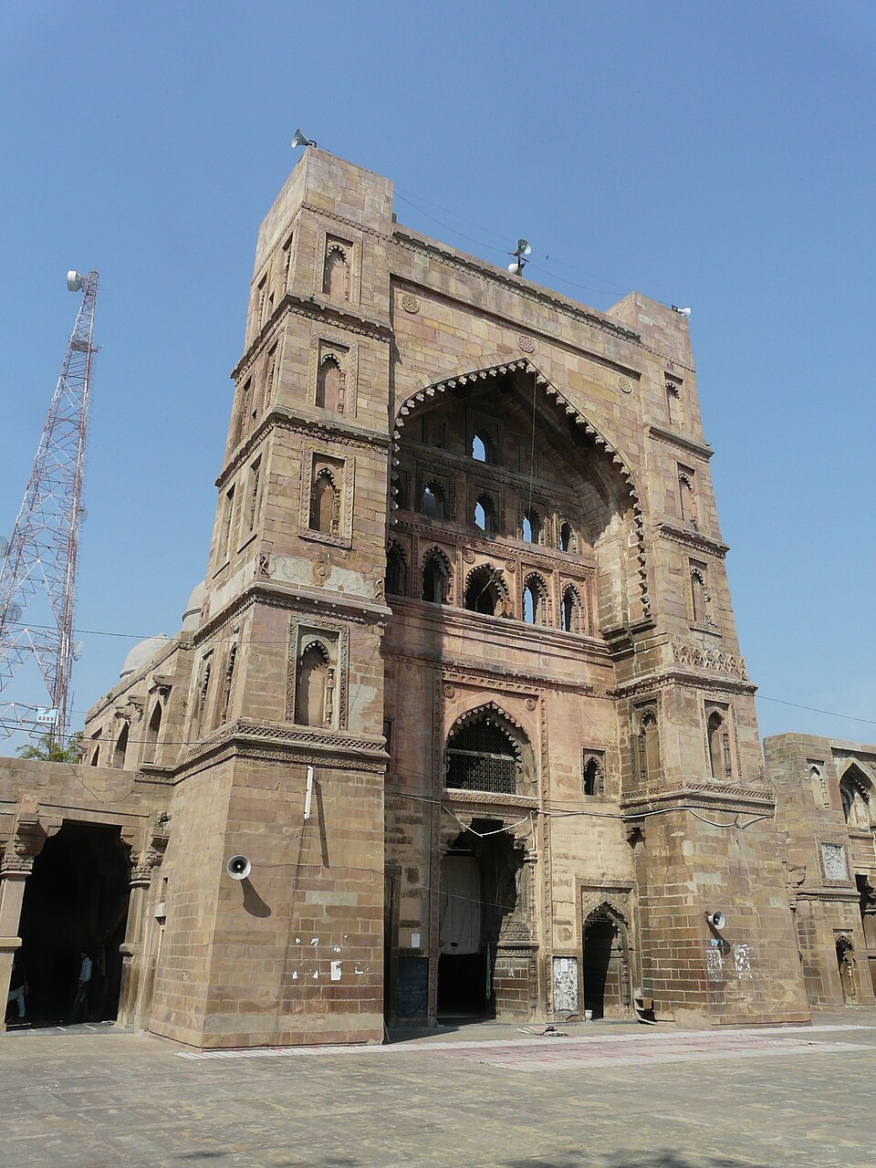The towering carved red-sandstone central gateway (pishtaq) of the Atala Masjid at Jaunpur, an example of Sharqi-dynasty architecture, under a clear blue sky.