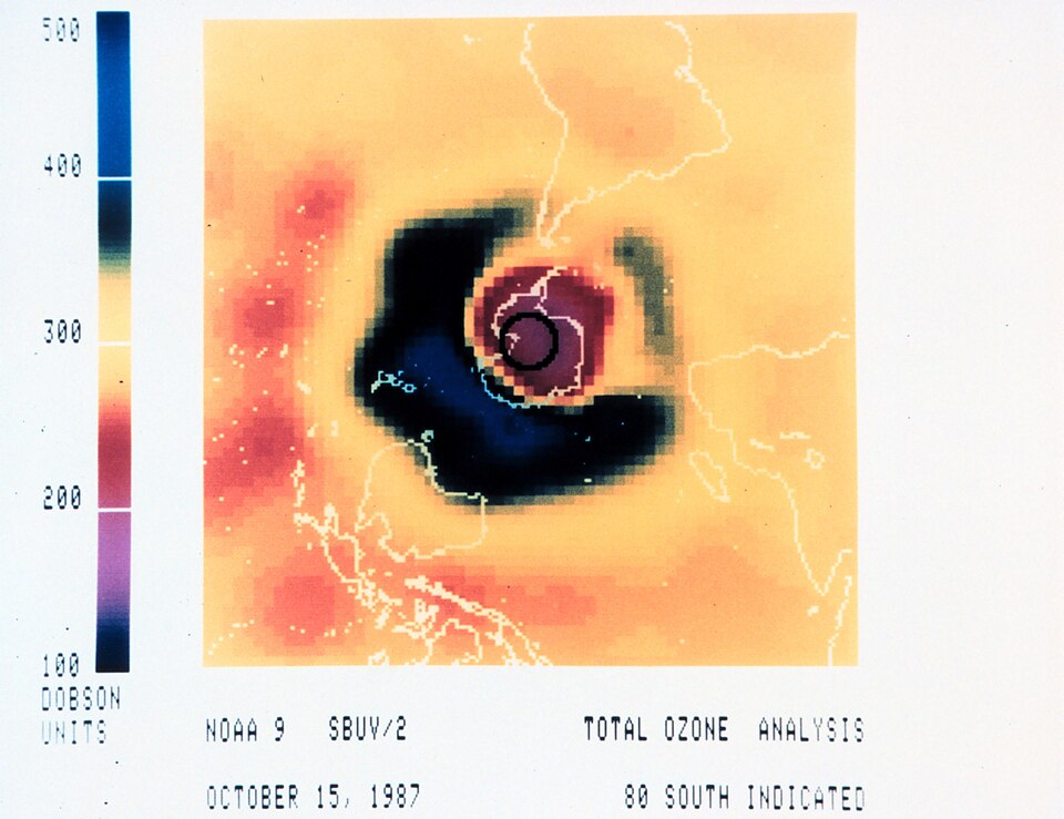 A NOAA false-colour satellite total-ozone image of the Southern Hemisphere showing the dark low-ozone Antarctic ozone hole, beside a Dobson-unit colour scale.