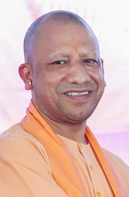 A smiling man with a shaved head wearing saffron-orange robes, photographed from the shoulders up.