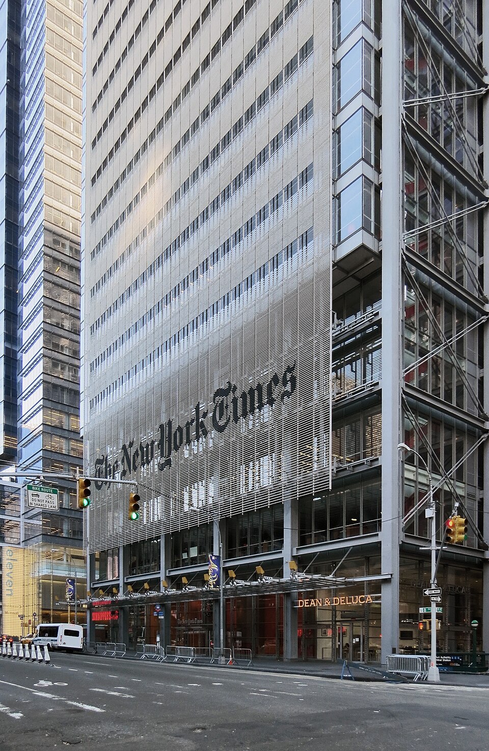 Street-level view of the New York Times Building in Manhattan, its glass-and-steel facade carrying the large gothic 'The New York Times' nameplate above the entrance.