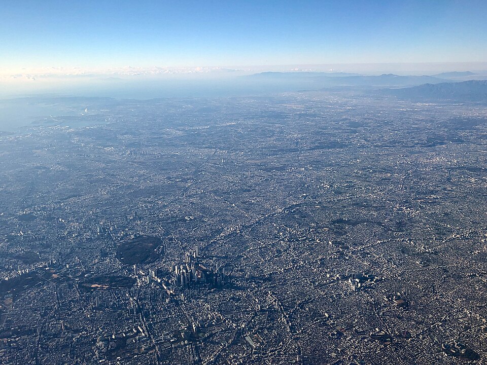 An aerial view of the vast, densely built-up Kanto Plain around Tokyo, flat urban sprawl stretching to distant hills and the sea.