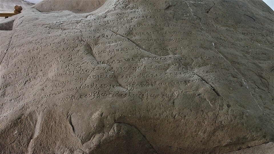 Rows of Brahmi characters chiselled across the rounded face of a large granite boulder