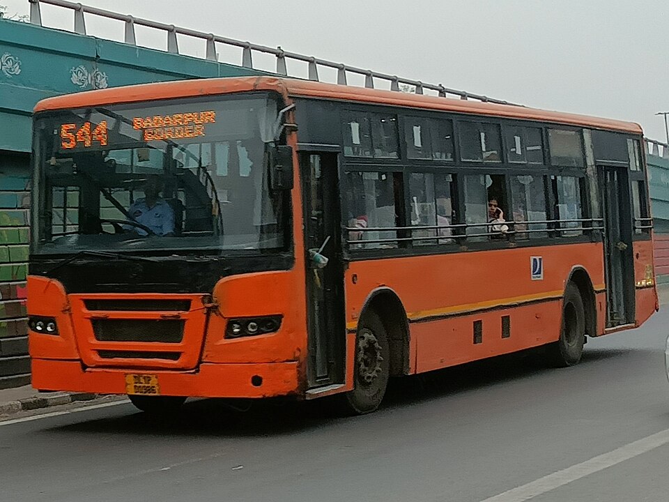 An orange CNG-powered Delhi cluster bus on route 544 to Badarpur Border travelling along a city road
