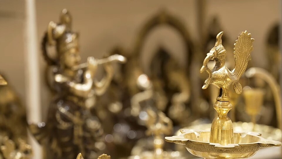 Polished brass handicrafts from Moradabad on display: a peacock-topped lamp in the foreground with cast brass figurines behind