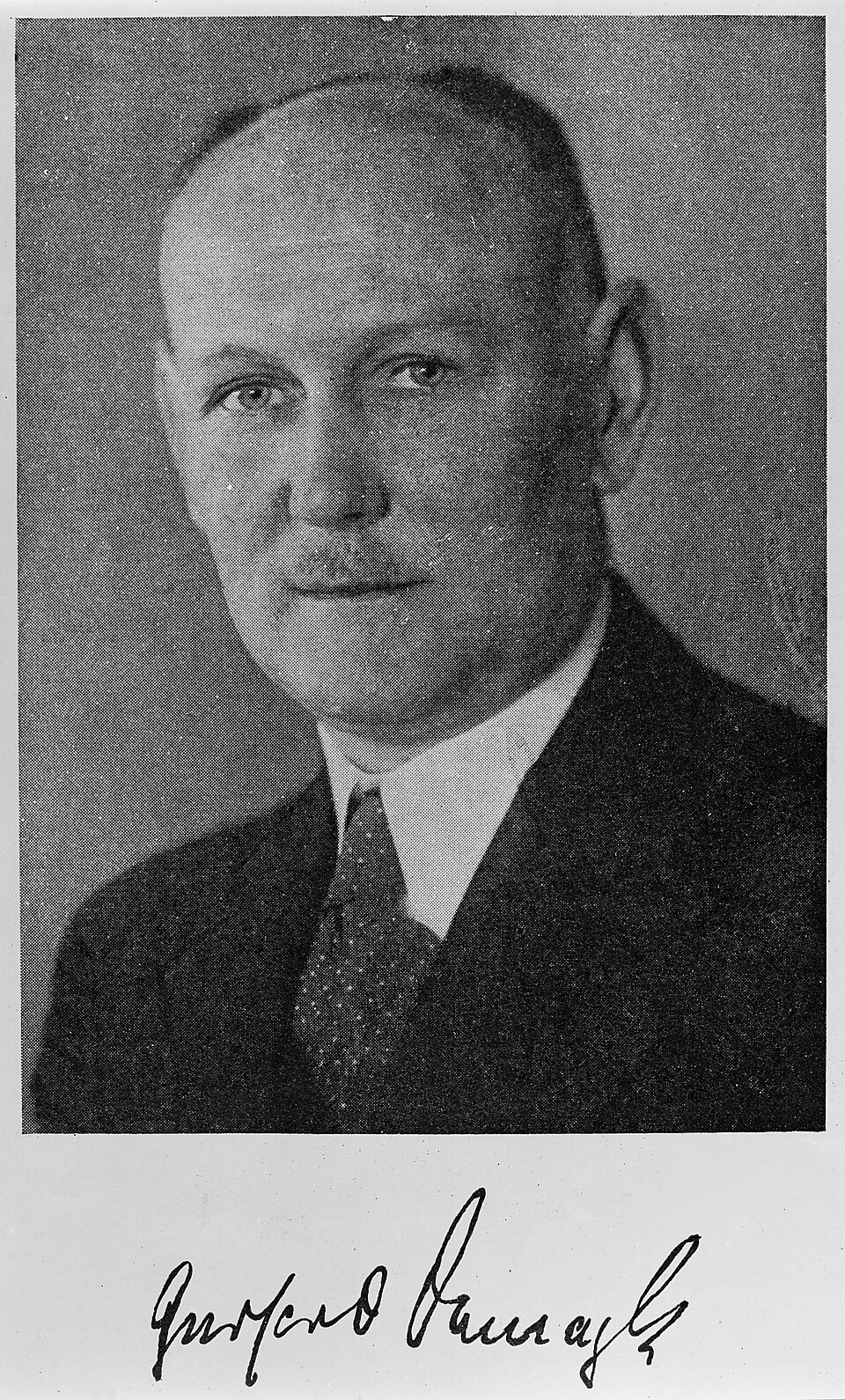 Black-and-white studio portrait of Gerhard Domagk in a dark suit and tie, with his handwritten signature printed below