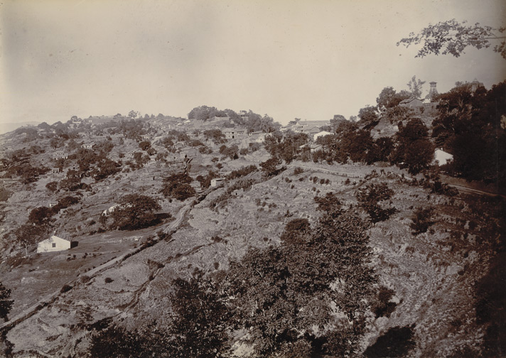 Historic sepia photograph of Almora, its houses scattered along a wooded ridge above terraced hillsides in the Kumaon hills